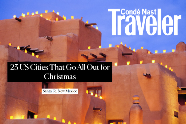 Bright luminarias sit atop an adobe clad building, text reads Conde Nast Traveler: 23 US cities that go all out for Christmas, Santa Fe New Mexico