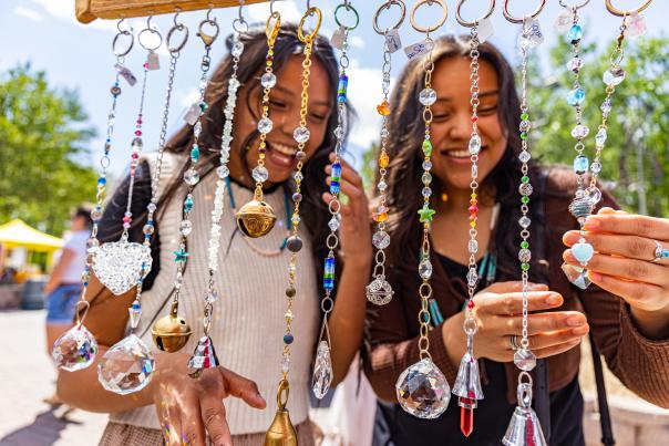 two smiling girls stand in front of a display of necklaces and pendants