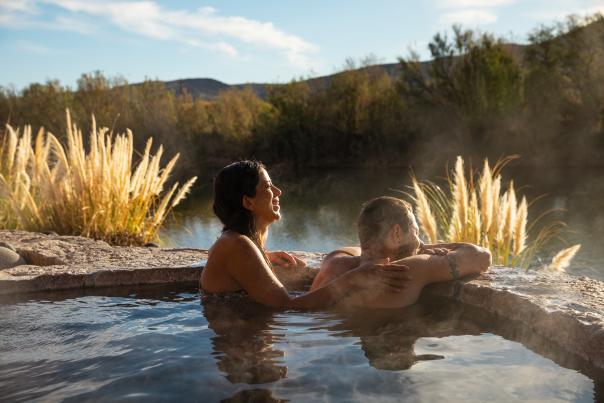 A couple smiles and relaxes in a private hot springs pool overlooking the Rio Grande River in Truth or Consequences, New Mexico.