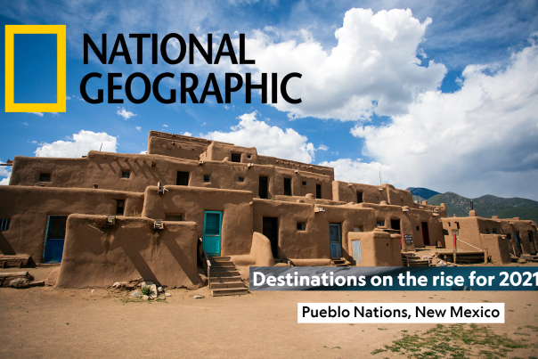 Ancestral pueblo dwellings feature adobe construction and blue doors sit before blue skies, text reads National Geographic, Destinations on the rise for 2021, Pueblo Nations, New Mexico