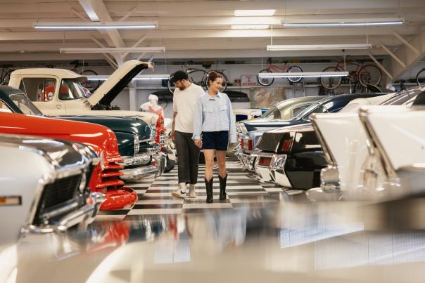 Two individuals walking through a vintage car exhibition, inspecting classic models closely.