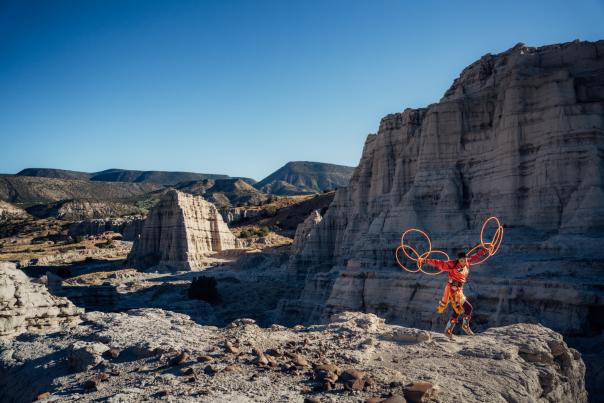 A traditional Native hoop dancer in a valley of rocks with mountains in the far distance