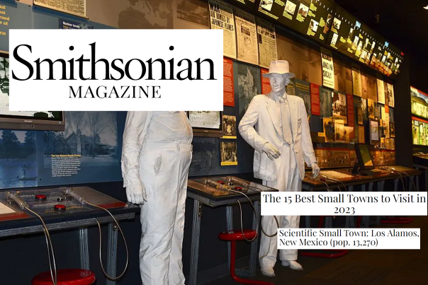 White sculptures of two people standing in front of a display about nuclear history. Text reads Smithsonian Magazine, The 15 Best Small Towns to Visit in 2023. Scientific Small Towns, Los Alamos New Mexico (pop 13,270)