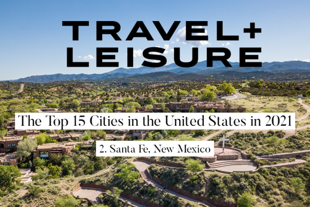 an aerial shot of a large cross on a hill, surrounded by pathways, shrubbery and mountains in the background. text reads Travel + Leisure top 15 cities in the United States in 2021, number 2 Santa Fe