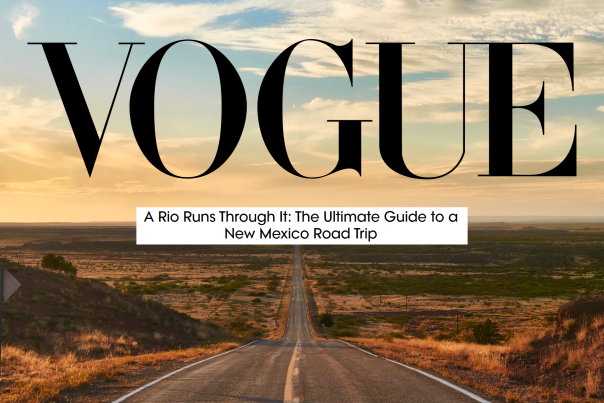 a two-lane road heads straight away from the camera through a desert plain, accented by green shrubbery. Text reads VOGUE, A Rio Runs Through It: The Ultimate Guide to a New Mexico Road Trip