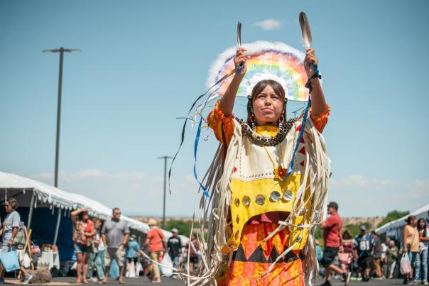 a native american woman in traditional garb burns ceremonial herbs and plants in front of a spectating crowd