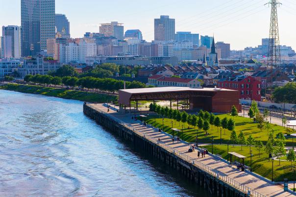 A drone shot of the French Quarter and New Orleans city skyline taken from over the MIssissippi River of the Goldring Woldenberg Riverfront Park at sunset.
