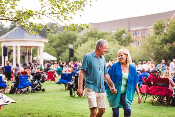 Couple holding hands at summer concert with gazebo stage in background