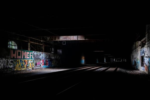 Dark abandoned railway tracks in a New York City tunnel with graffiti on the walls and sunlight filtering through in the distance