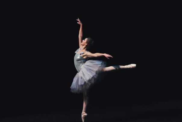Ballerina mid-leap in a flowing white costume during a classical ballet performance on stage