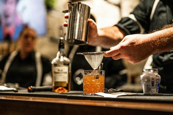 Bartender pouring a whiskey cocktail at a dark bar counter — tipping bartenders 20% or more is standard NYC etiquette