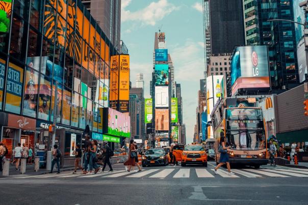 Pedestrians crossing a busy intersection in Times Square surrounded by Broadway theater billboards and yellow taxis in New York City