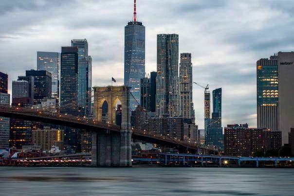 Brooklyn Bridge spanning the East River at dusk with the illuminated Manhattan skyline rising in the background