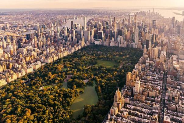 Golden-hour aerial view of Central Park's full expanse of autumn trees and The Lake surrounded by Manhattan skyscrapers, with Lower Manhattan visible in the distance