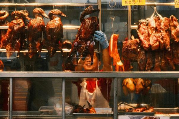 Whole roasted ducks hanging in rows at a Chinatown meat shop window, a daily staple for local shoppers