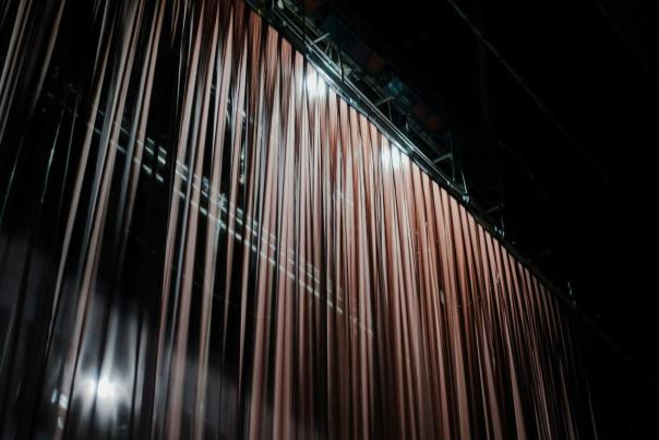Closed stage curtain in a dark theater, matching the backstage Broadway theme