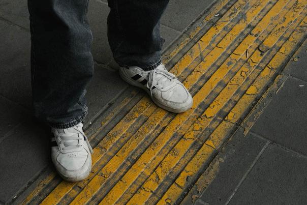 Worn white sneakers standing on a weathered yellow tactile strip on an urban transit platform