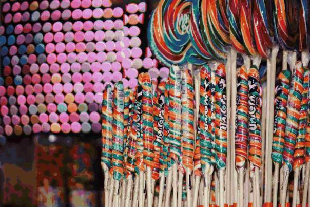 Colorful rainbow lollipops and candy sticks displayed against glowing neon lights inside a vibrant candy-themed attraction in Times Square.