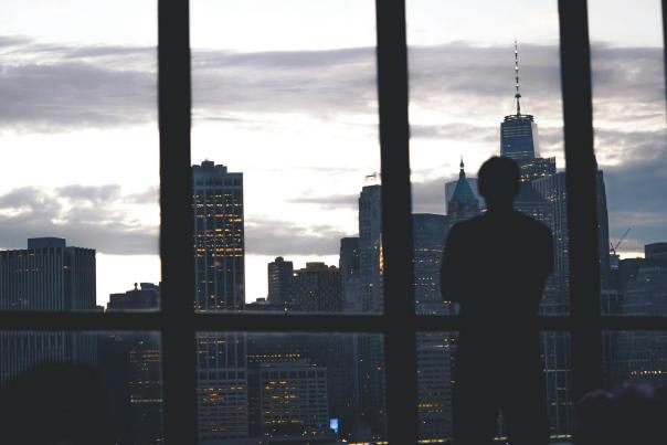 A person standing by a floor-to-ceiling window in a Manhattan apartment overlooking the city skyline at dusk