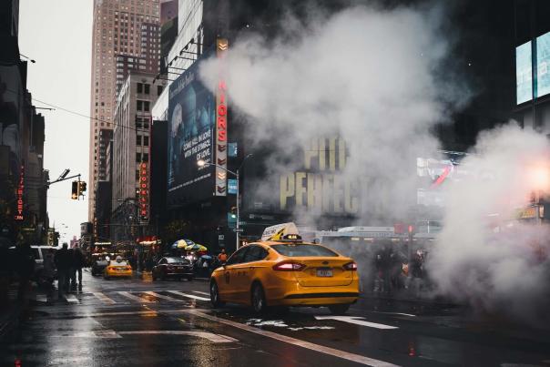 Steam rising from an underground vent on a Manhattan street with a yellow taxi cab passing through the white plume