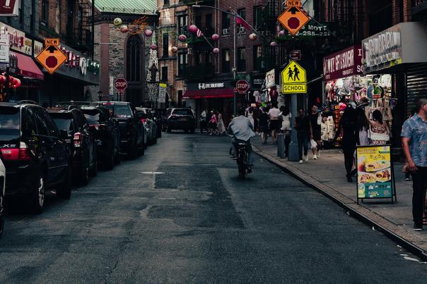 Pedestrians walking along Mott Street in NYC's Chinatown, lined with storefronts, Chinese signage, and hanging lanterns