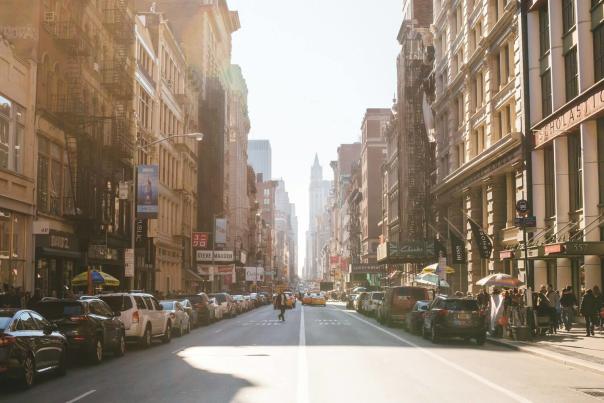 Busy Manhattan street lined with shops and pedestrians bathed in warm sunlight with skyscrapers visible in the distance in New York City