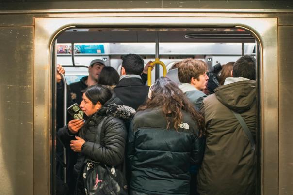Commuters packed tightly into a crowded New York City subway car during rush hour, pressing against the doors in winter coats