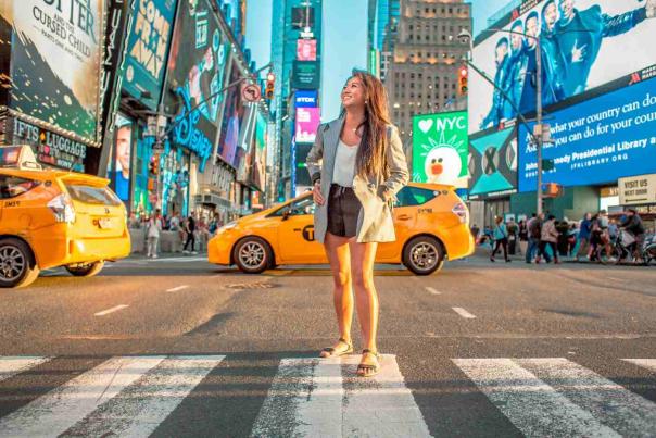 Woman standing in the middle of Times Square surrounded by yellow taxis, neon billboards, and evening crowds in New York City.