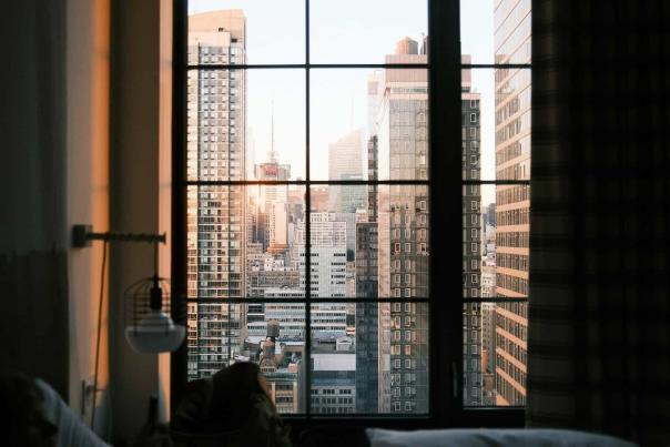 NYC skyscrapers bathed in warm sunset light as seen from a hotel room window, blending the comfort of the room with the energy of the city outside