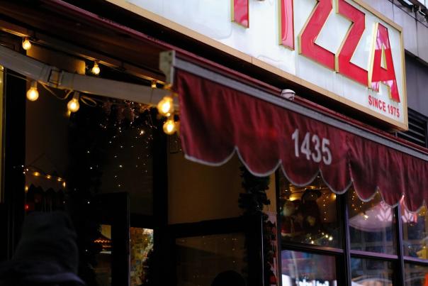 A hand holding a large New York-style pizza slice, the quintessential street food of the city