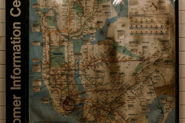 NYC subway system map posted on a station wall in moody green lighting, a key navigation tool for phone-free travelers