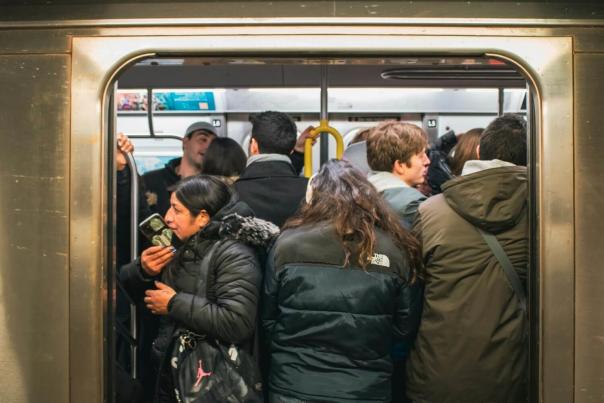 A packed New York City MTA subway train with passengers standing tightly together during a crowded rush hour commute