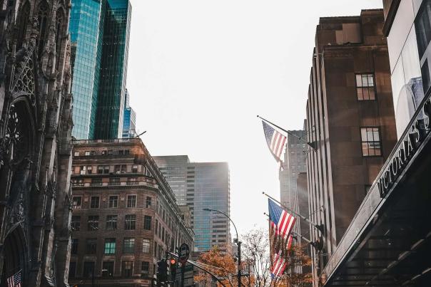 Pedestrians walking down a sunlit Manhattan sidewalk flanked by tall skyscrapers on a clear day