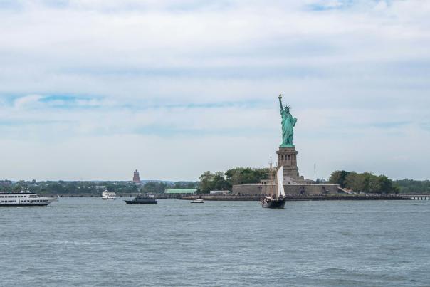 The Statue of Liberty standing on Liberty Island in New York Harbor seen from the water with boats nearby on a clear day