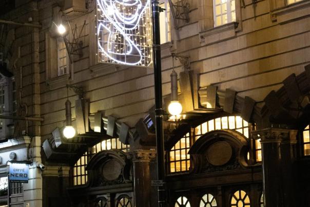 Ornate theater entrance decorated with glowing comedy and drama mask lights against a dark urban night backdrop