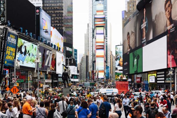 Large crowds of people walking through Times Square in New York City surrounded by towering digital billboards, theaters, and heavy traffic.