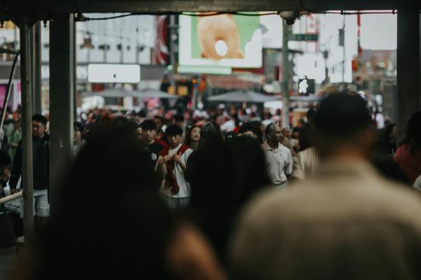 Dense crowd of tourists and pedestrians packed shoulder-to-shoulder on Times Square, with bright LED billboards glowing in the background