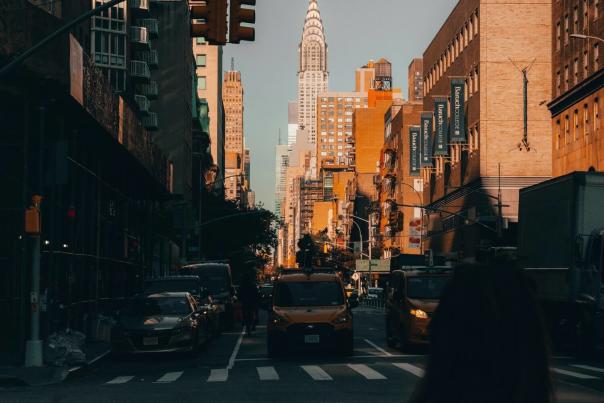 A woman crossing a Midtown Manhattan street alone with the Chrysler Building rising in the background and yellow taxis nearby