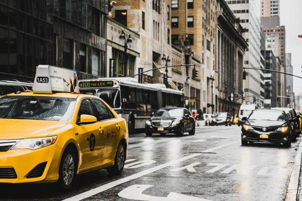 Yellow NYC taxi cab moving through busy Manhattan street traffic past brownstone buildings