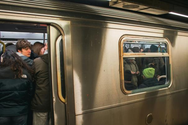 Packed New York City subway car with standing passengers during a busy rush hour commute, doors open