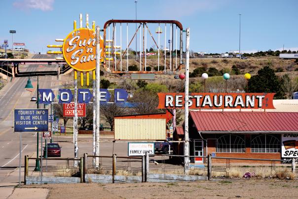 Vintage roadside scene with vibrant "MOTEL" and "RESTAURANT" signs, evoking nostalgia. Desert landscape and a highway add to the retro vibe.