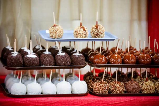 A variety of candy apples on tiered trays, featuring toppings like nuts, chocolate, and caramel.