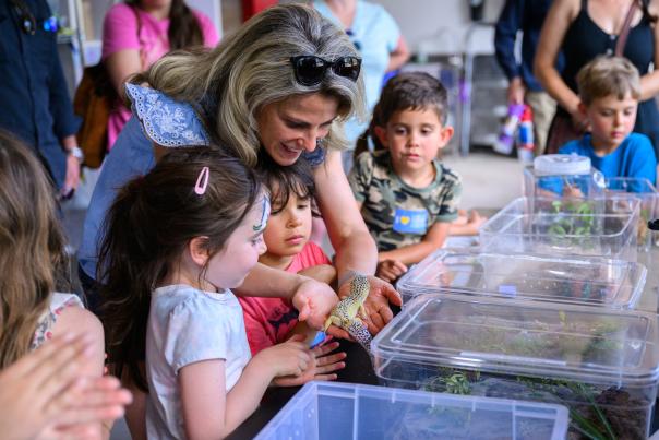 Adult helping children with a hands-on activity at a community event.