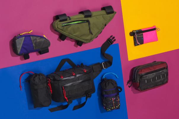 Seven colorful bags in different styles and sizes lay on a pink, blue, and orange background.