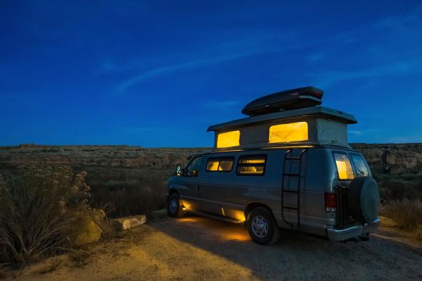 A camper van with illuminated interior lights parked in a desert landscape at twilight.