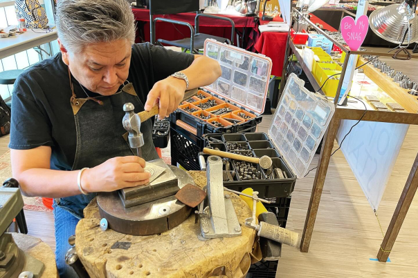 Lyndon Tsosie demonstrates Navajo metal stamping, using a hammer and tools at his workbench during a gem show.