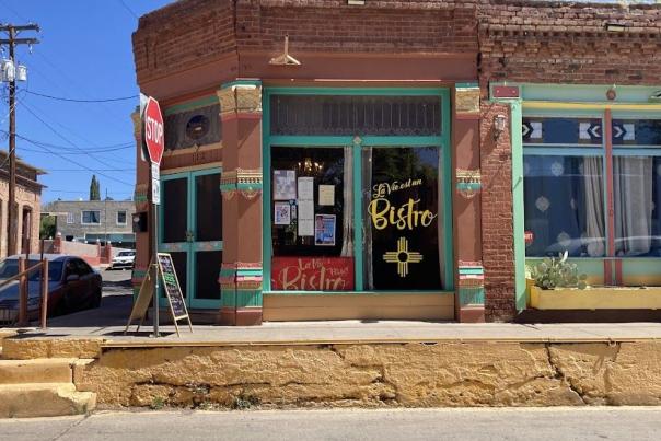 A colorful corner bistro with green and brown painted brick, signs in the window, and a stop sign outside.