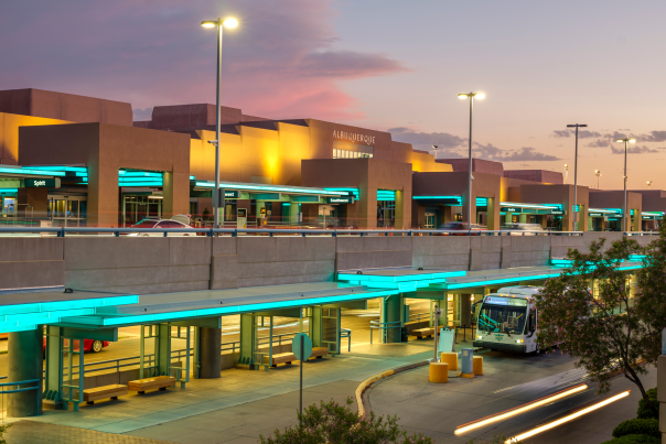 Albuquerque Sunport exterior at sunset with lit-up entrance and shuttle buses.