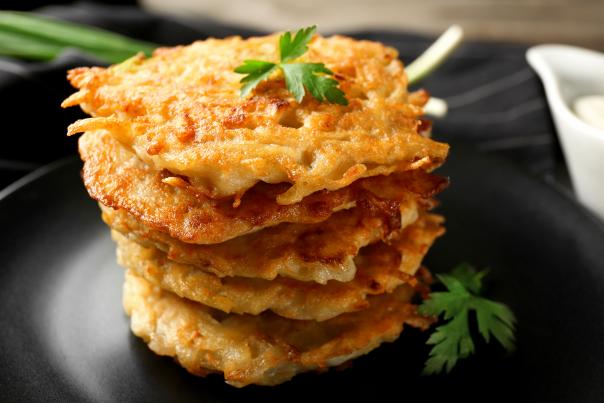 A stack of golden brown potato pancakes topped with parsley sits on a black plate.