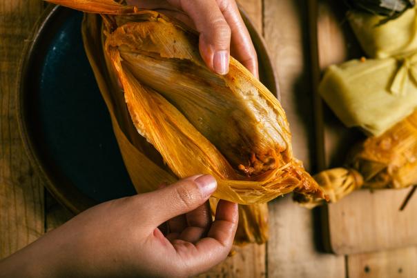 Person opening a tamal with his hands.